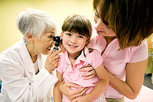 Healthcare professional examines child's ear, while being held by mother