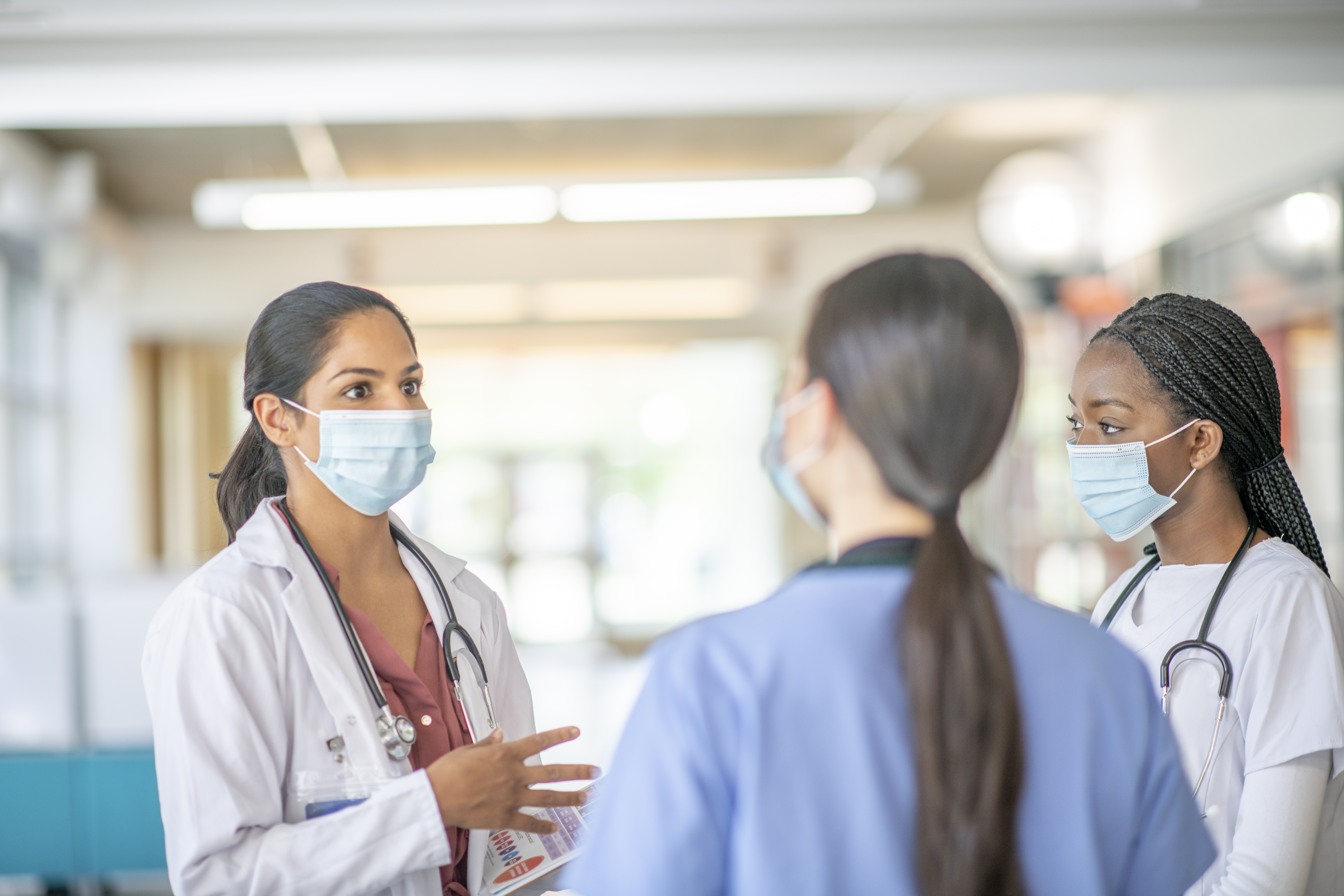 Trois jeunes travailleuses de la santé portant un masque se concertent dans un hôpital.