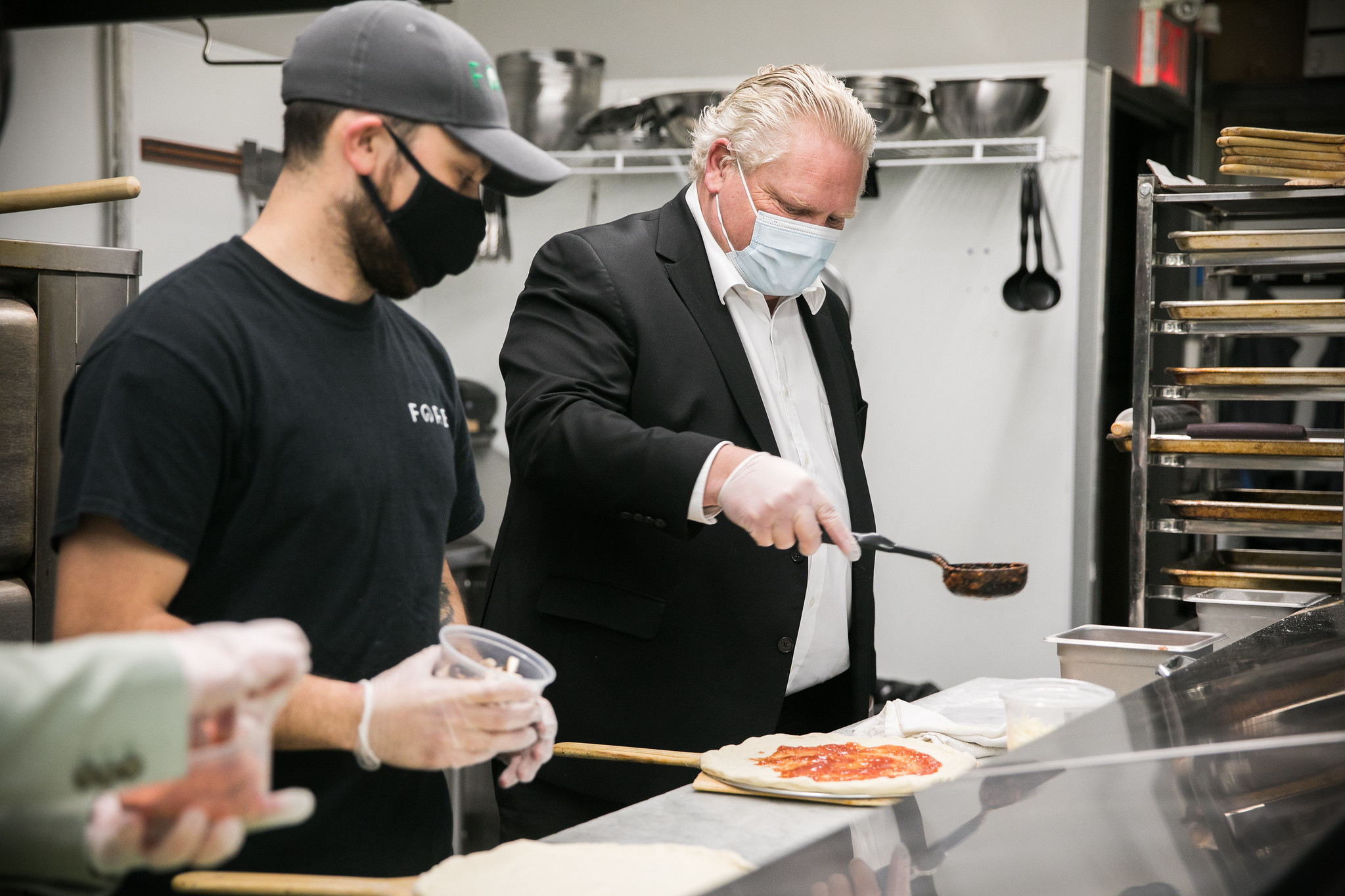 Le premier ministre apprenant à faire de la pizza en compagnie d'un employé de restaurant.