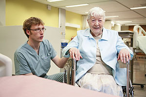 Une patiente âgée en fauteuil roulant au côté d'une professionnelle de la santé, dans un hôpital