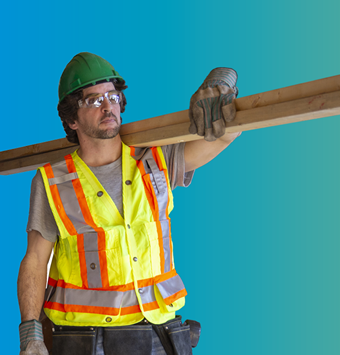 Photo of a construction worker carrying lumber.