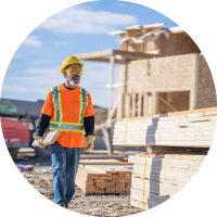 Photo of a worker carrying lumber at a housing construction site.