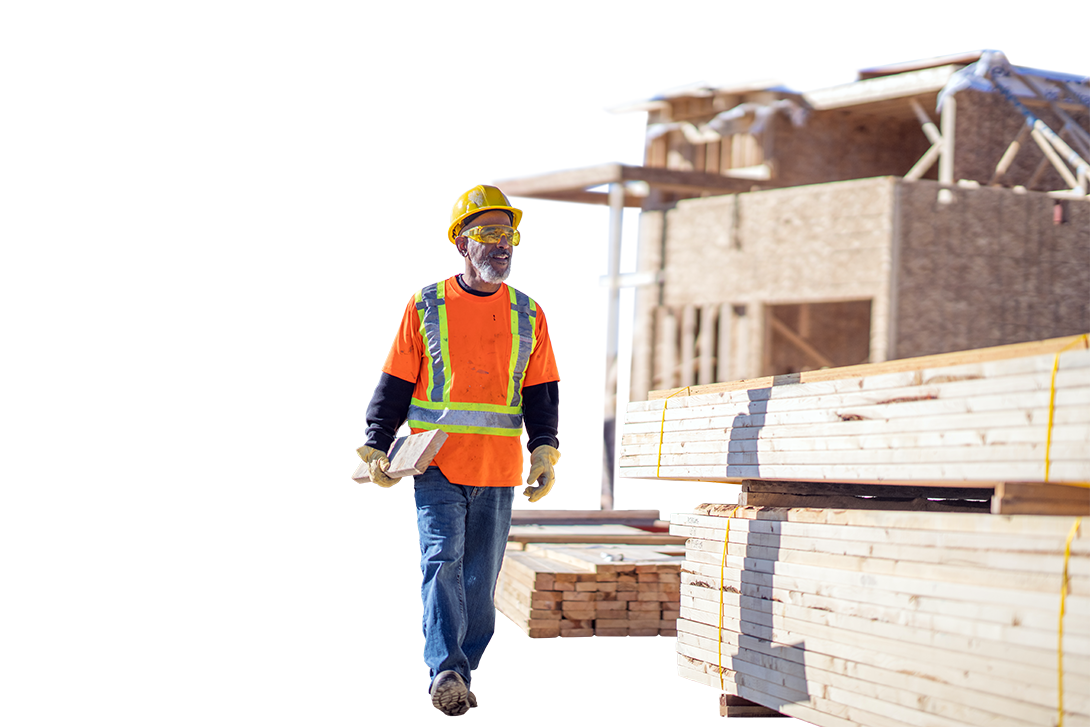 Photo of a worker carrying lumber at a housing construction site.