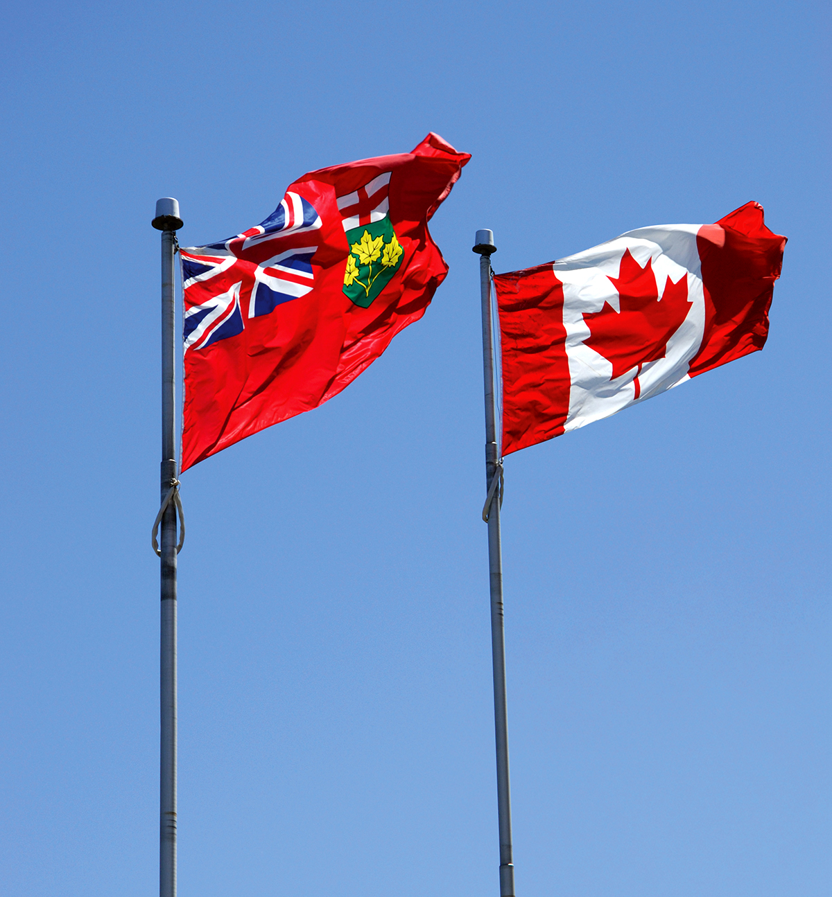 Photo of province of Ontario and Canada flags under clear blue skies.