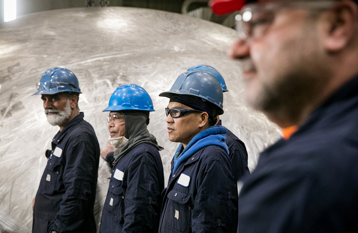 Photo de travailleurs portant des casques protecteurs, debout dans une installation industrielle.
